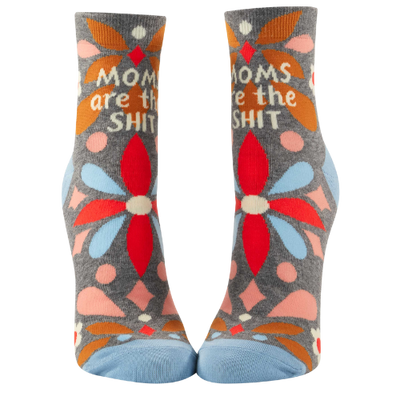 A pair of playful ankle socks by Blue Q, featuring the phrase "Moms Are The Shit" in bold, fun lettering. The design includes vibrant colors, whimsical patterns, and charming details, perfect for celebrating moms with a sense of humor and style.